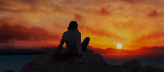 a Young man sit on top of mountains top edge at sunset time admiring the beauty of nature.
