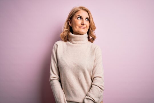 Middle age beautiful blonde woman wearing casual turtleneck sweater over pink background smiling looking to the side and staring away thinking.