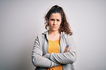 Obraz premium Young beautiful sportswoman with curly hair wearing sportswear over white background skeptic and nervous, disapproving expression on face with crossed arms. Negative person.