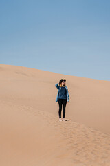 A travel girl is standing in the middle of a sand dune. A traveler in a black hat and blue skirt in Death Valley National Park