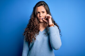 Young beautiful woman with curly hair wearing blue casual sweater over isolated background mouth and lips shut as zip with fingers. Secret and silent, taboo talking