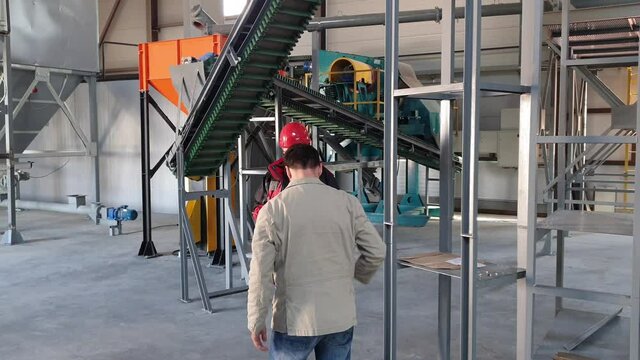 engineer and factory Director discuss production against the background of a working conveyor at the factory, a worker in a hard hat and overalls