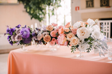 Presidium, banquet table with a pink tablecloth. Plates and cutlery, purple glasses, napkins, candles in glass candlesticks. Bouquet of flowers, asters, roses, carnations, eustomas.