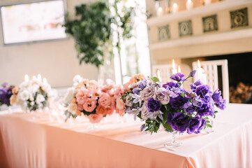 Presidium, banquet table with a pink tablecloth. Plates and cutlery, purple glasses, napkins, candles in glass candlesticks. Bouquet of flowers, asters, roses, carnations, eustomas.