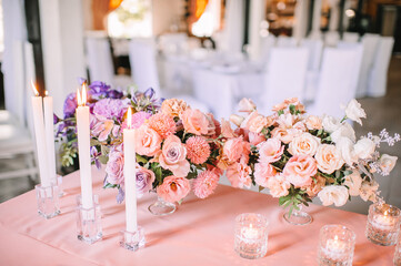 Presidium, banquet table with a pink tablecloth. Plates and cutlery, purple glasses, napkins, candles in glass candlesticks. Bouquet of flowers, asters, roses, carnations, eustomas.