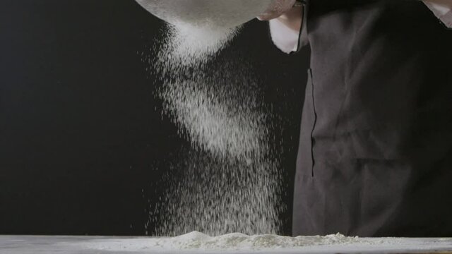 Falling slowly flour on a wooden dark table from sifter on a black background. Slow motion, Full HD video, 240fps, 1080p. Process preparing of homemade pastry.