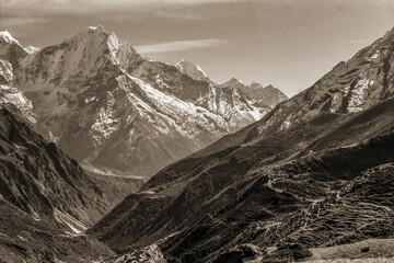 Fototapeta na wymiar Colossal snowy mountains and deep valleys amid the Himalayas. The world largest and highest mountain range, in northern Nepal. Black and white photo.