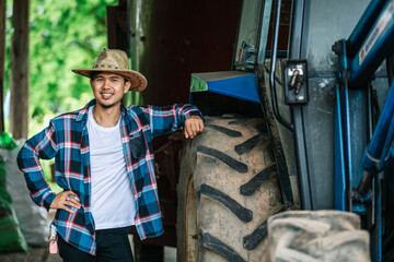 Portrait of a handsome asian young farmer standing in a shirt and smiling at the camera, on a tractor and nature background. © tong2530
