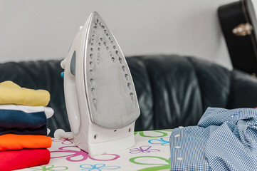 Electric iron and pile of clothes on blurred background