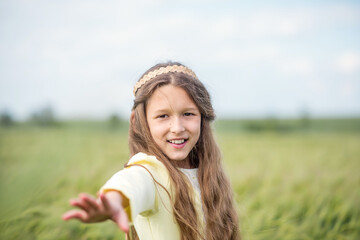 Green wheat field. Beautiful girl walks in the field. A child with a basket collects spikelets. Recreation and agriculture. Long hair of a young girl