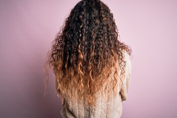 Young beautiful woman with curly hair wearing casual sweater standing over pink background standing backwards looking away with crossed arms