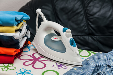 Electric iron and pile of clothes on blurred background