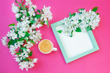 Light green photo frame decorated with flowers of an apple tree on a pink background. A cup of morning coffee, an apple tree branch. Wooden frame for text.