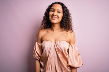 Young beautiful woman with curly hair wearing casual t-shirt standing over pink background with a happy and cool smile on face. Lucky person.