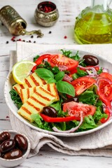 Delicious salad with grilled halloumi cheese, lettuce, tomatoes, bell pepper, red onion, Kalamata olives, olive oil, Basil, lemon and spices. Mediterranean cuisine. Selective focus