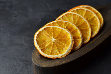Organic homemade dried orange chips slices in wooden plate on dark background