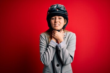 Young beautiful blonde motorcyclist woman wearing motorcycle helmet over red background shouting and suffocate because painful strangle. Health problem. Asphyxiate and suicide concept.