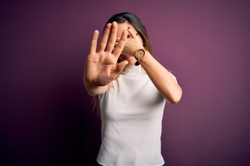 Young beautiful blonde woman with blue eyes wearing casual t-shirt over purple background covering eyes with hands and doing stop gesture with sad and fear expression. Embarrassed and negative