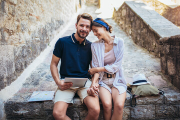 Romantic tourist couple sitting on stairs using digital tablet.