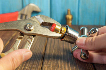 The master plumber repairs the tap with a wrench, the working environment in the workshop