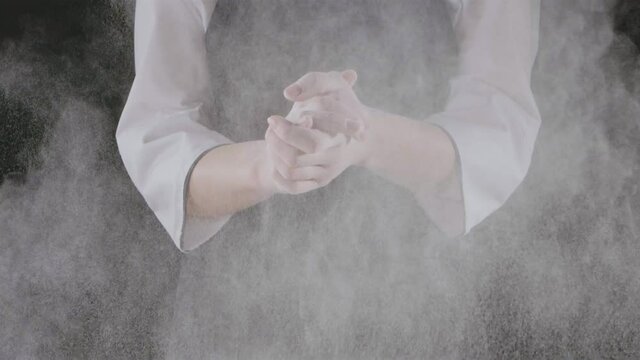 Chef is clapping his hands filled with flour on a black background. Slow motion, Full HD video, 240fps, 1080p. Process preparing of homemade pastry.