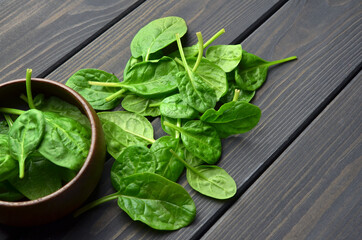 Fresh spinach leaves in wooden bowl on dark rustic background. Healthy vegan food concept. Eco-conscious vegan lifstyle.