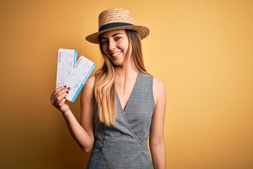 Young blonde tourist woman with blue eyes on vacation wearing hat holding boarding pass with a happy face standing and smiling with a confident smile showing teeth