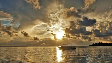 Naklejka na ściany i meble Fantastic golden sunset in the Maldives. The setting sun shines through the picturesque clouds and turns everything golden. The surface of the ocean is like molten metal. Boat on the sunny track.