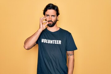Young handsome hispanic volunteer man wearing volunteering t-shirt as social care mouth and lips...