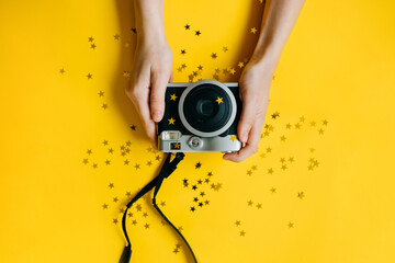 Close up of woman hands holding a instant film camera with golden stars on yellow background.