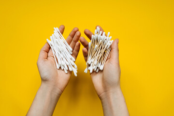 Human hands holding plastic and organic wooden cotton swabs on a bright yellow background. Concept of taking care of the environment.