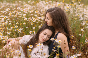 Two girls in dark blue and white dresses in sunny day sitting in chamomile field - 354058432