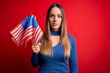 Young blonde patriotic woman holding usa flag on independence day on 4th of july with a confident expression on smart face thinking serious