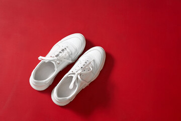 New white trendy sneakers for women on red wall background.
