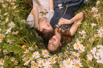 Two girls with closed eyes in dark blue and white dresses in sunny day lying down in chamomile field - 354058882