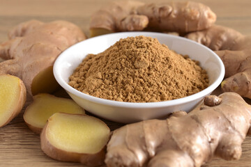 Ginger powder in a white bowl and fresh ginger root on a wooden background.