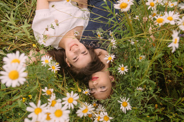 Two girls in dark blue and white dresses in sunny day lying down in chamomile field - 354059012