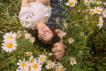 Two girls with closed eyes in dark blue and white dresses in sunny day lying down in chamomile field - 354059020