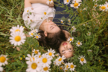 Two girls with closed eyes in dark blue and white dresses in sunny day lying down in chamomile field