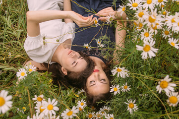 Two girls in dark blue and white dresses in sunny day lying down in chamomile field