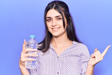 Young beautiful girl holding bottle of water smiling happy pointing with hand and finger to the side