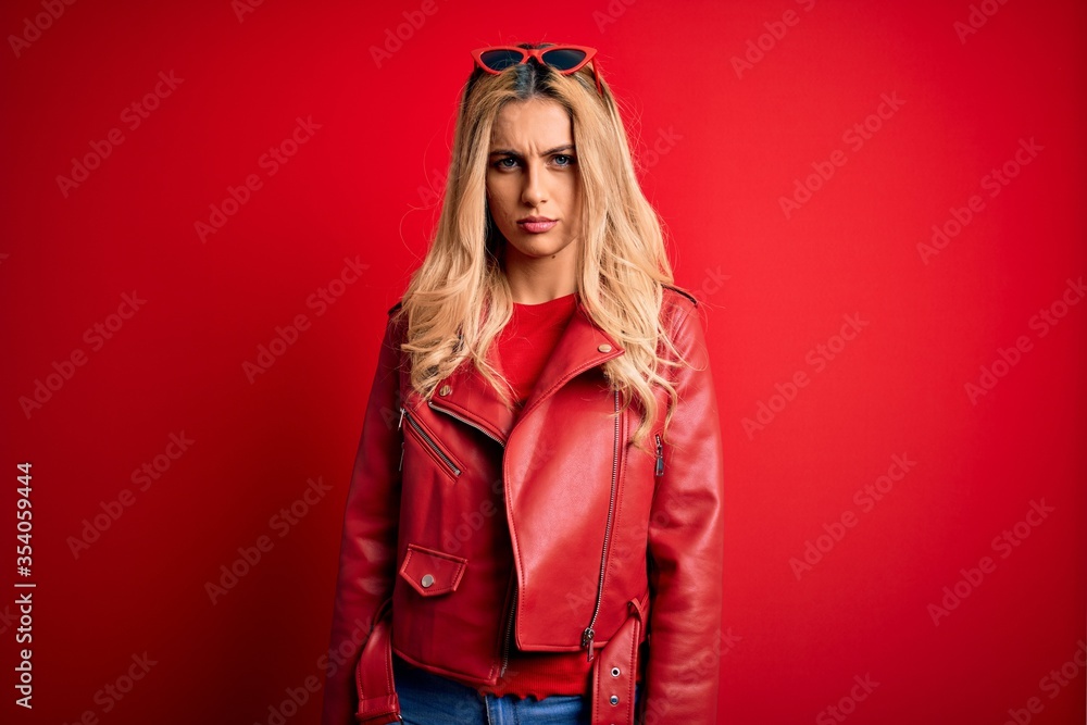 Sticker young beautiful blonde woman wearing casual jacket standing over isolated red background skeptic and