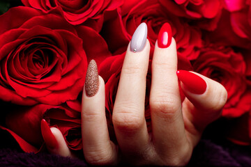 Girl's hand with a beautiful manicure in red, gold and gray colors against a background of red roses