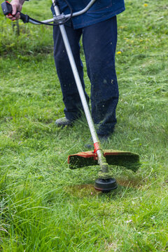 a worker mows grass and weeds with a lawn mower in the country