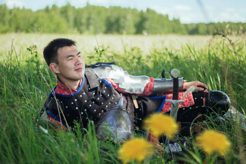 A medieval Asian warrior in armor is resting while sitting in tall grass.