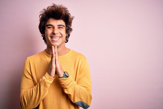 Young handsome man wearing yellow casual t-shirt standing over isolated pink background praying with hands together asking for forgiveness smiling confident.