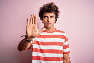 Young handsome man wearing striped casual t-shirt standing over isolated pink background doing stop...