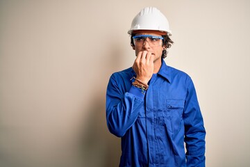 Young constructor man wearing uniform and security helmet over isolated white background looking stressed and nervous with hands on mouth biting nails. Anxiety problem.