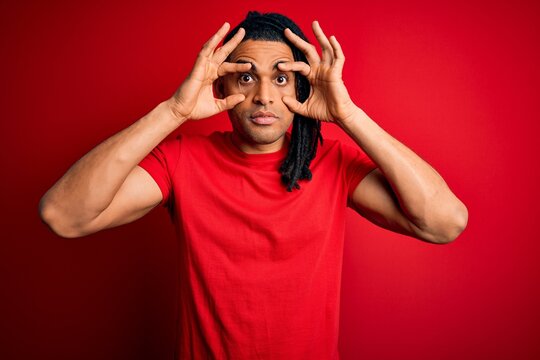 Young handsome african american afro man with dreadlocks wearing red casual t-shirt Trying to open eyes with fingers, sleepy and tired for morning fatigue