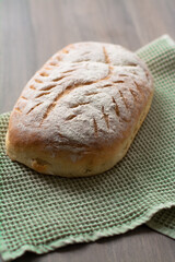 Homemade artisan sourdough bread loaf with artistic leaf pattern scoring and a wavy line in the middle on a green kitchen towel on wooden surface. Rustic aesthetic 
